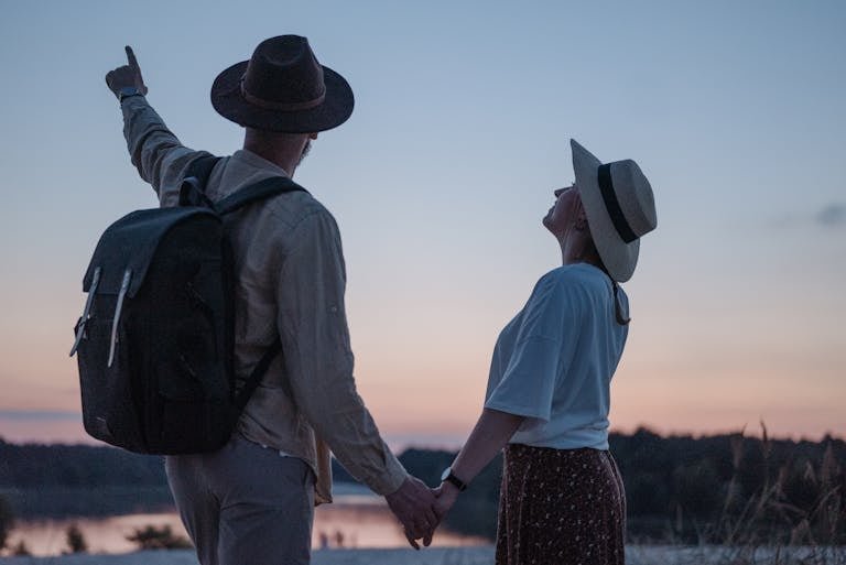 Romantic couple holding hands while watching a sunset at a serene lakeside location, embracing nature.