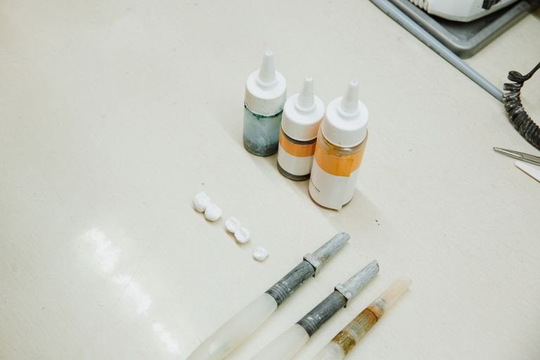 From above of various medical bottle and tubes for making denture and fake teeth placed on white table in dental clinic